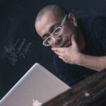 Man on an Apple laptop in front of a chalkboard