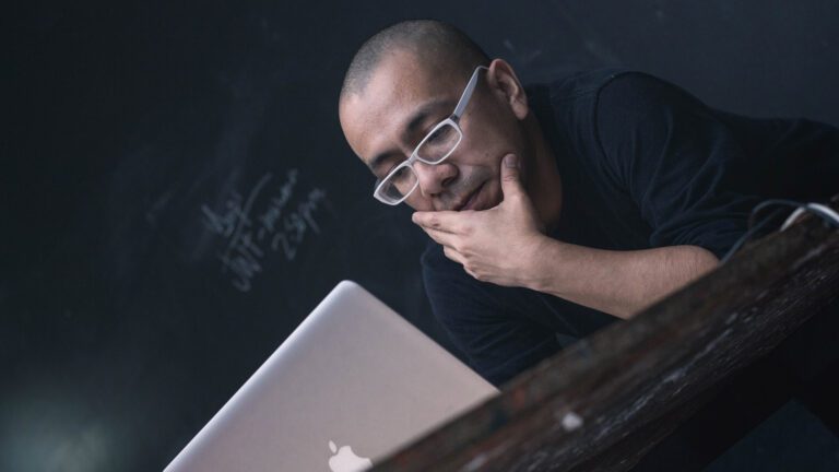 Man on an Apple laptop in front of a chalkboard