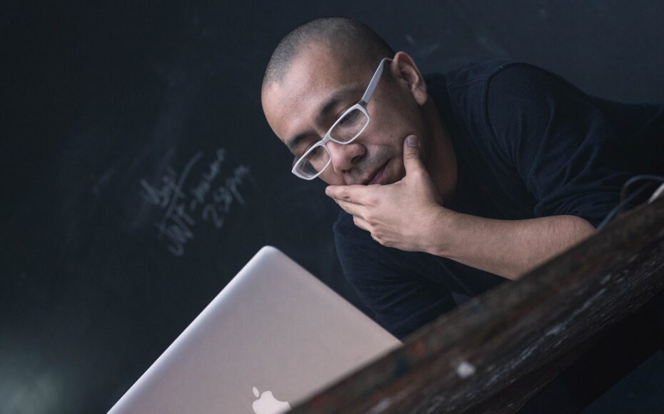 Man on an Apple laptop in front of a chalkboard