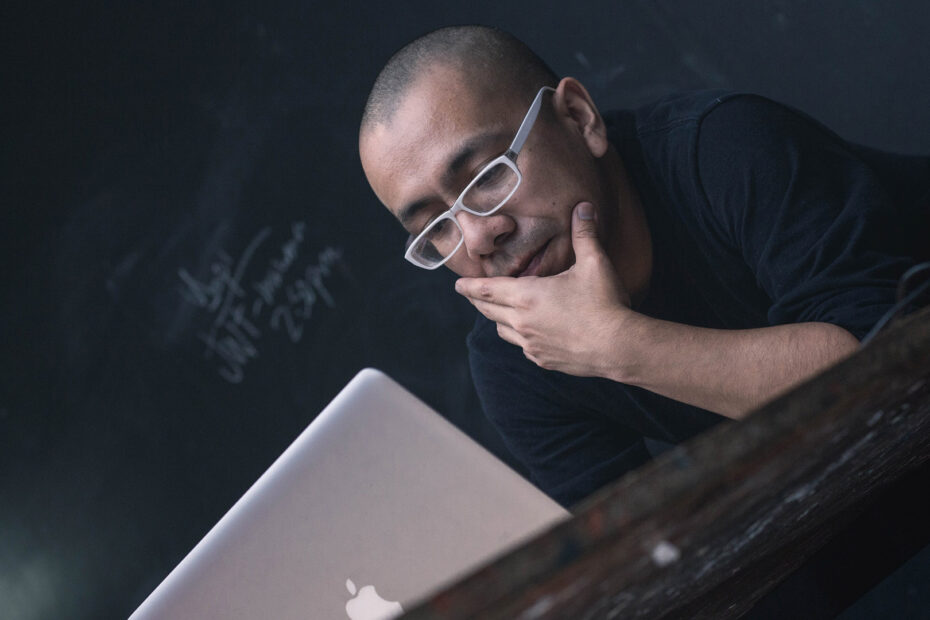 Man on an Apple laptop in front of a chalkboard