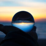 Person holding a crystal ball up to the sunrise on a beach