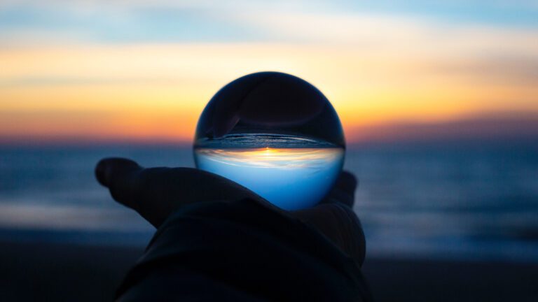 Person holding a crystal ball up to the sunrise on a beach