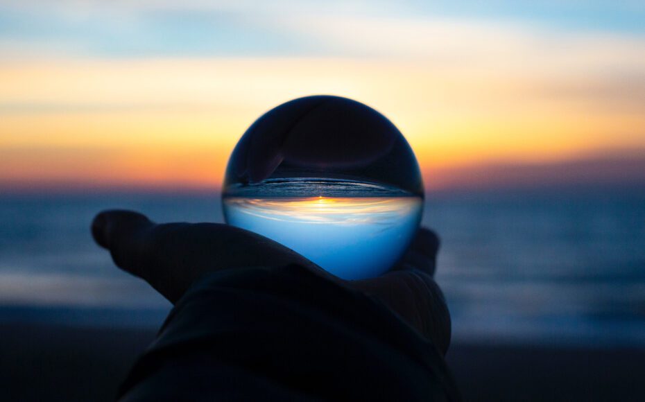 Person holding a crystal ball up to the sunrise on a beach