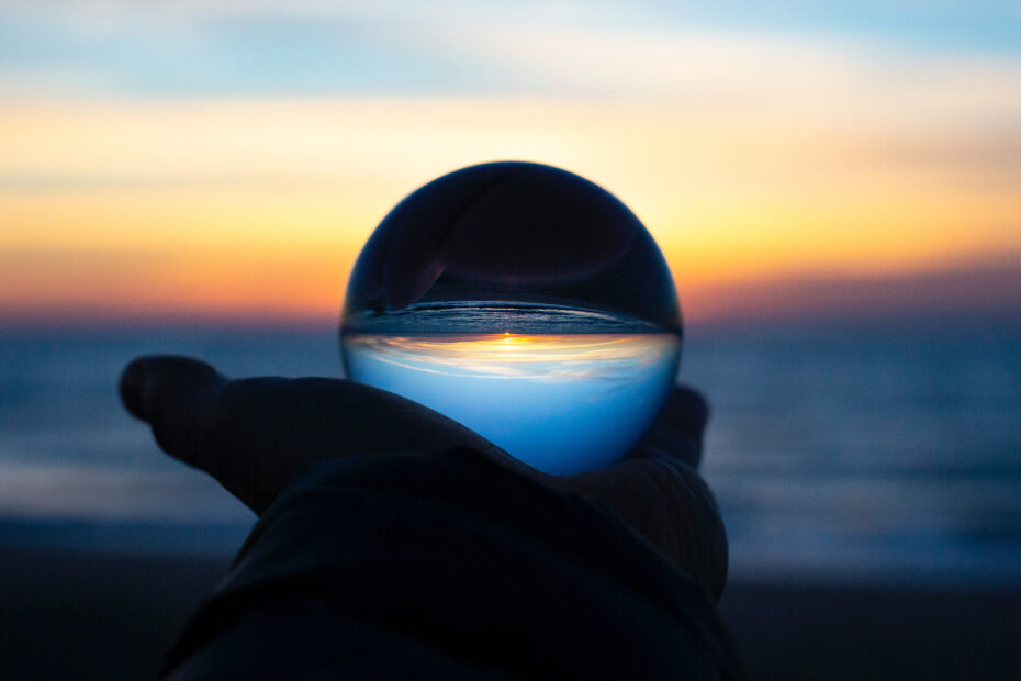 Person holding a crystal ball up to the sunrise on a beach